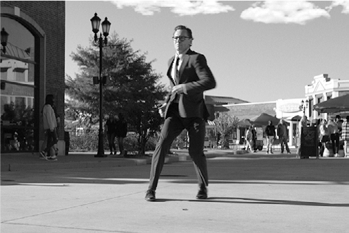 Chuck’s right leg is blurred forward, left leg bent back, arms swinging outward on a outdoor plaza.