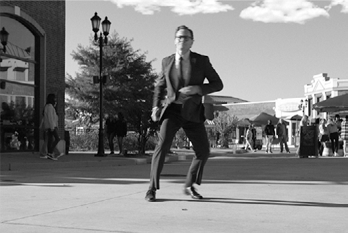 Chuck is also airborne, but with legs bent at a different angle, arms positioned for balance, on a outdoor plaza.