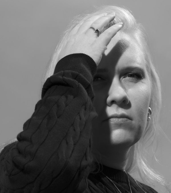 A blackandwhite photo of a blonde person with their hand raised to their forehead.